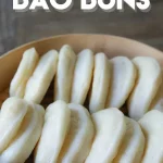 A wooden bowl containing creamy white steamed buns folded in round halves.