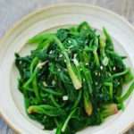 Bright green sautéed spinach with garlic in a white bowl on a grey tablecloth.