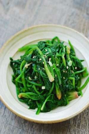 Bright green sautéed spinach with garlic in a white bowl on a grey tablecloth.