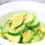 Bright green and yellow stir fried zucchini are piled in a while bowl, and garnished in sesame seeds.