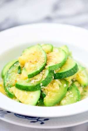 Bright green and yellow stir fried zucchini are piled in a while bowl, and garnished in sesame seeds.
