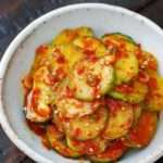 Cucumbers thinly sliced and covered in red chilis in a white bowl