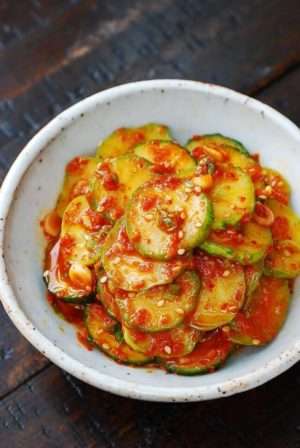 Cucumbers thinly sliced and covered in red chilis in a white bowl